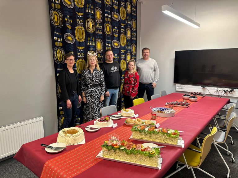 Office workers stand around table with Christmas cakes and treats.
